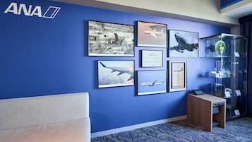 A blue wall with framed aviation-related pictures, a wooden desk, and a glass display case with items.