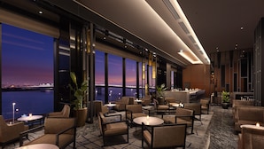 Eine moderne Hotelhalle mit Blick auf die Stadtlandschaft im Abendrot, ausgestattet mit gemütlichen Sitzbereichen und einer Bar.