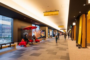 A modern indoor space with benches and a red umbrella, a sign for 'Villa Fontaine', and a 'Haneda Airport Garden' banner.