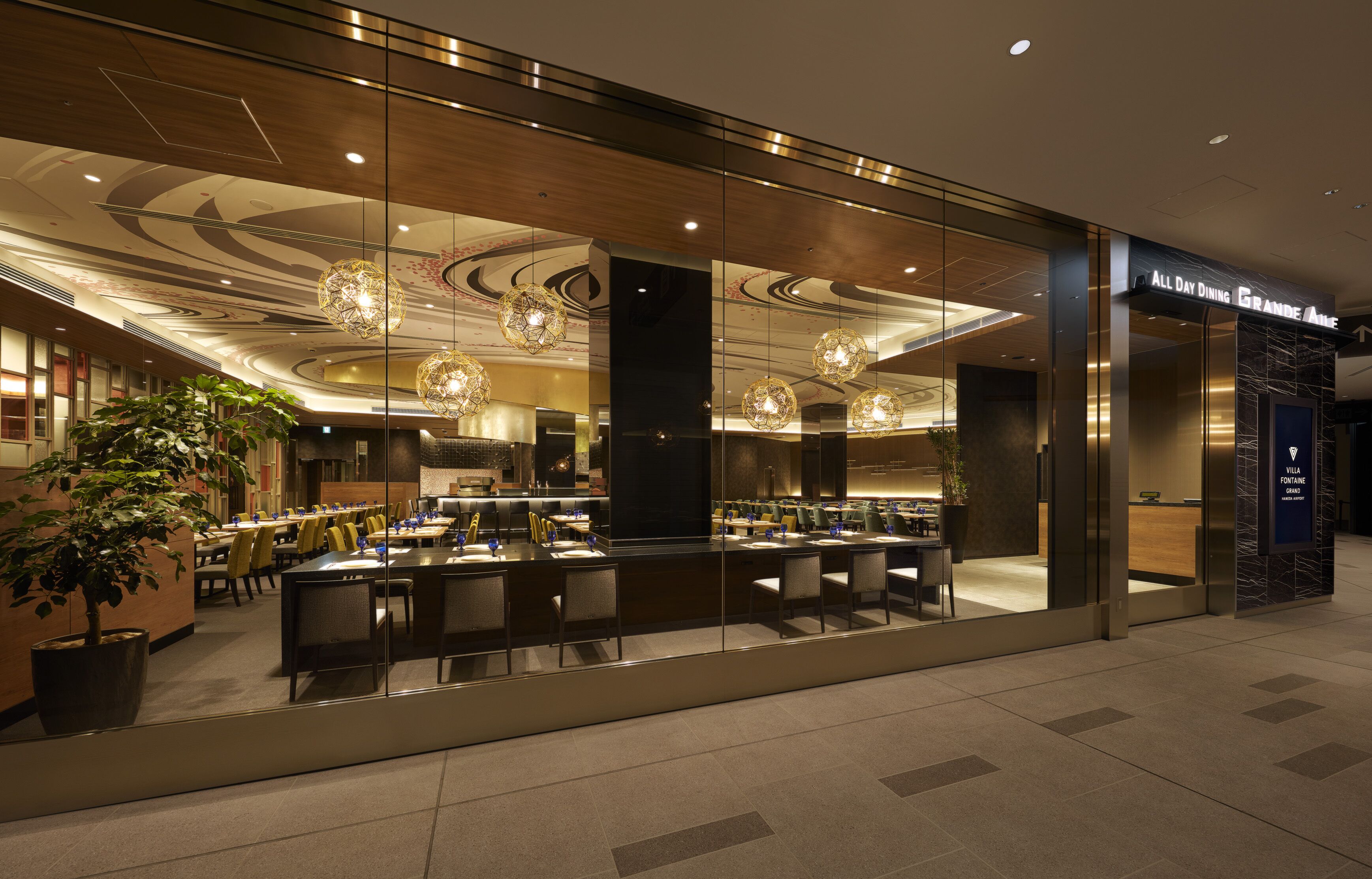 Un restaurante moderno con fachada de vidrio, iluminación interior y un letrero que indica 'All Day Dining'.