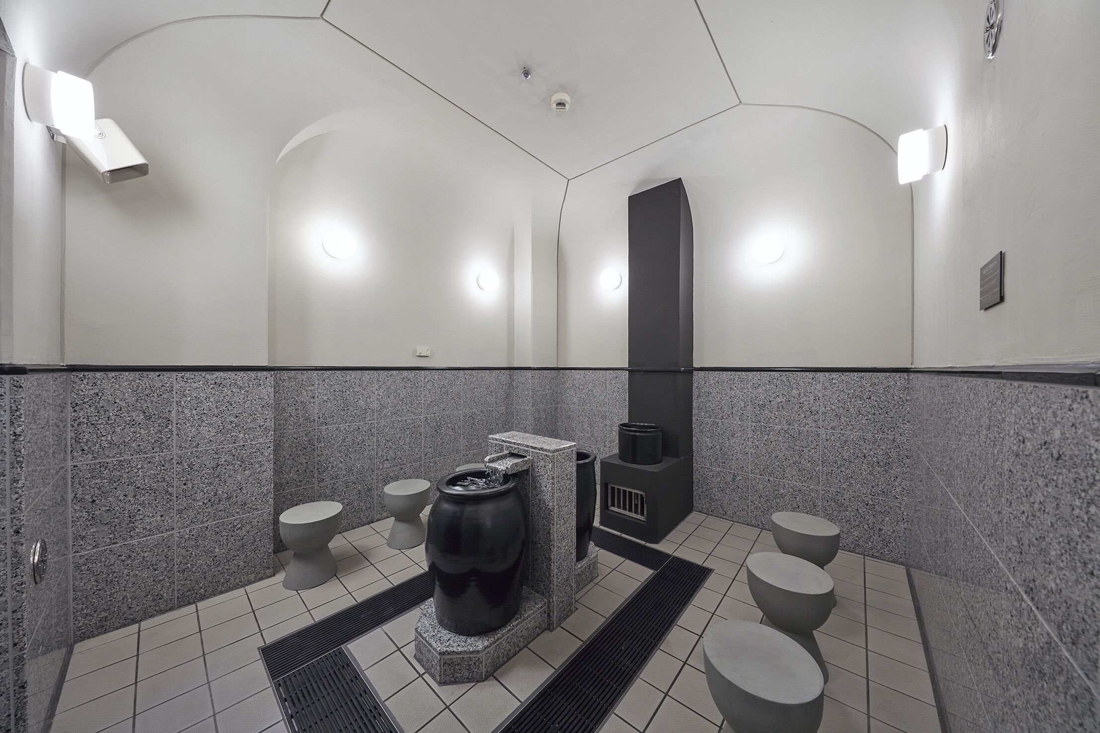A modern bathroom with a stone-tiled floor, a central water feature, and a black sink.