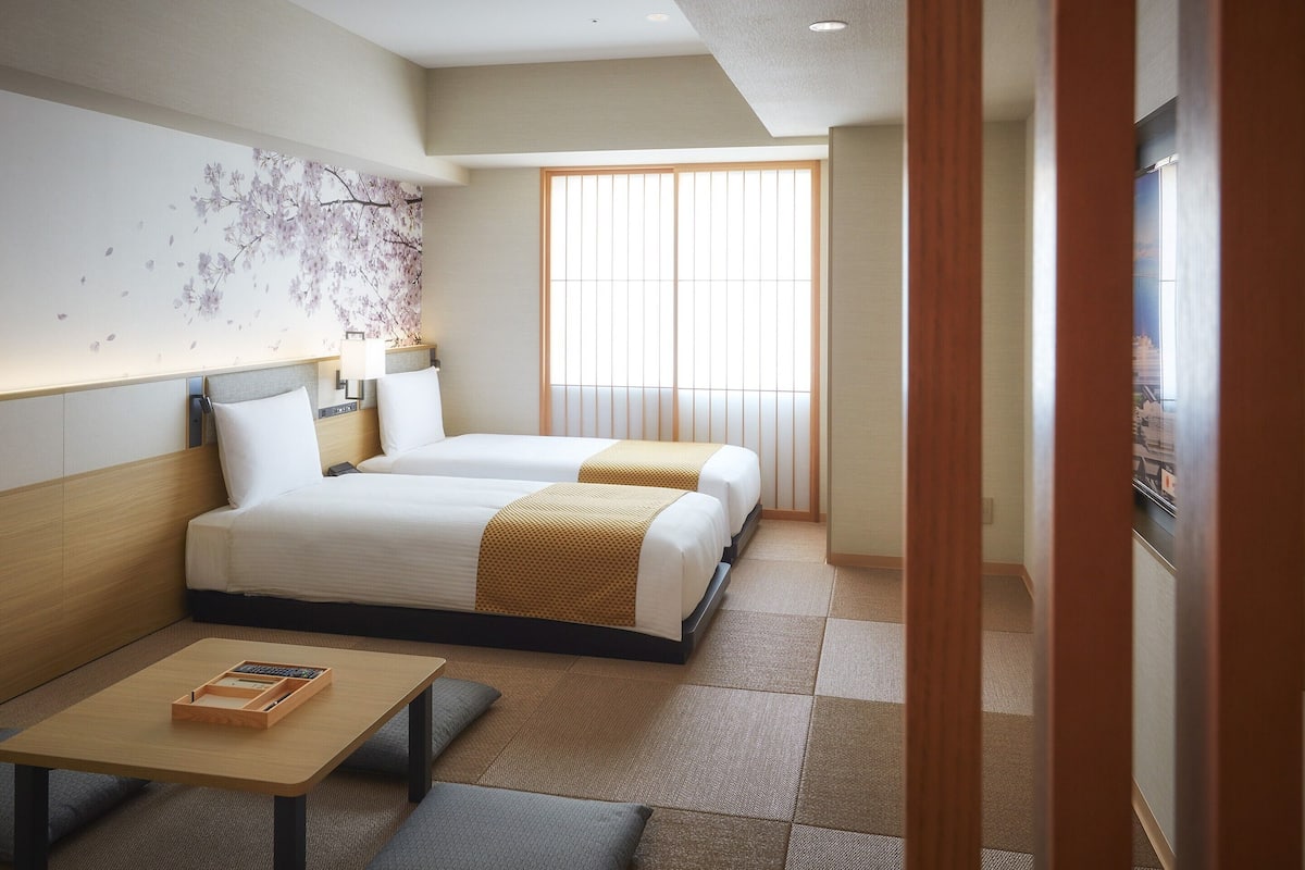 Ein Hotelzimmer mit zwei Betten, einem kleinen Tisch und einem Fenster mit Jalousien.