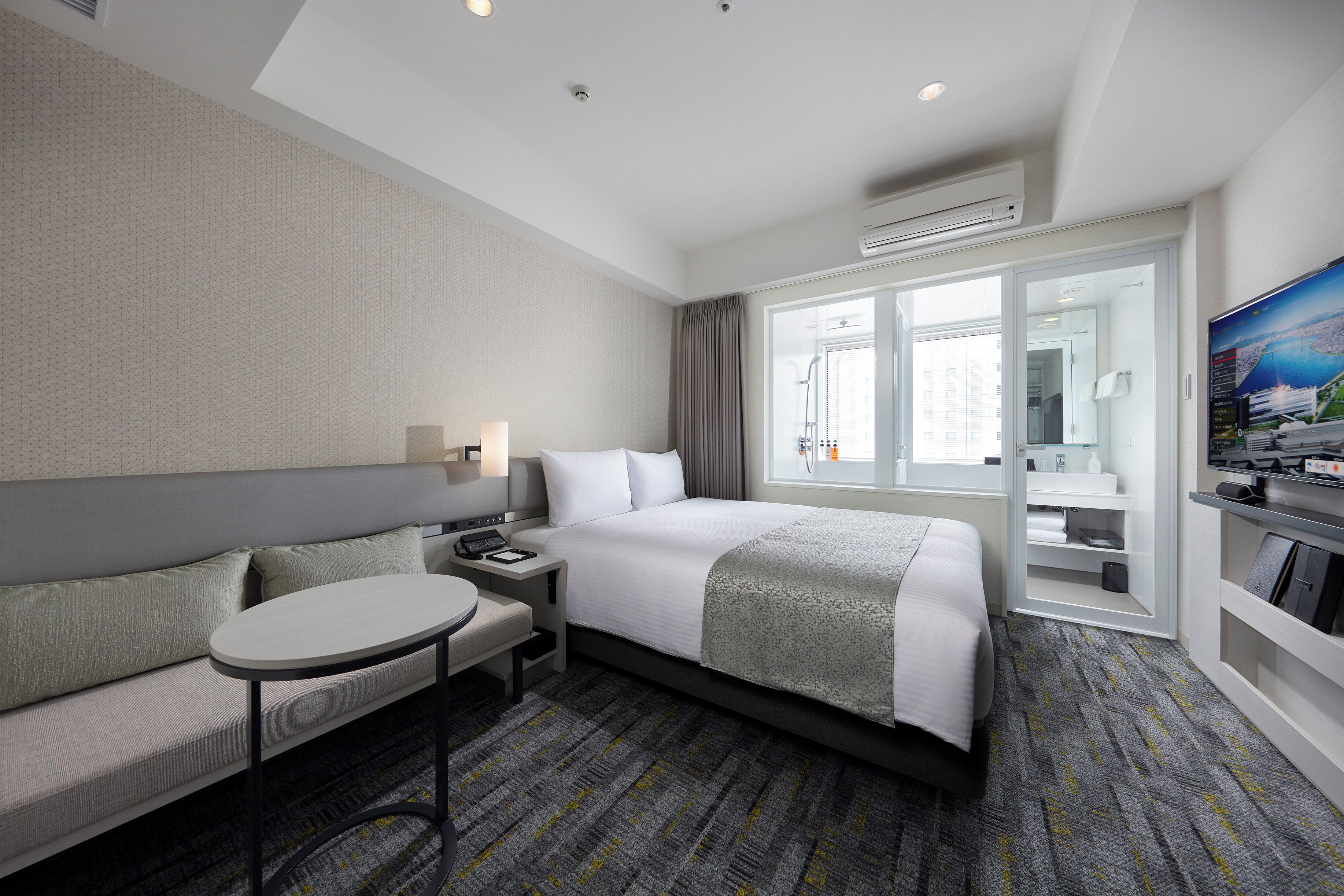 A hotel room with a bed, a sofa, a small table, a TV, and a window with a view.