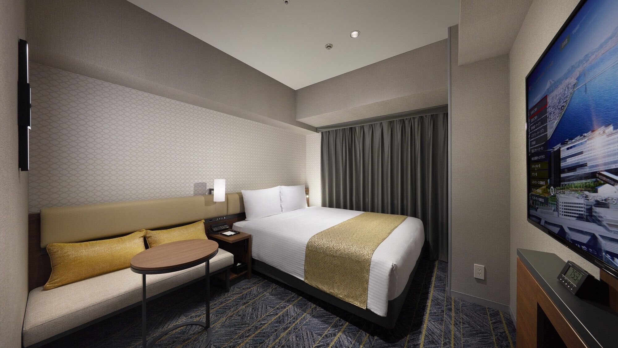 A hotel room with a bed, a sofa, a small table, a TV, and a nightstand.