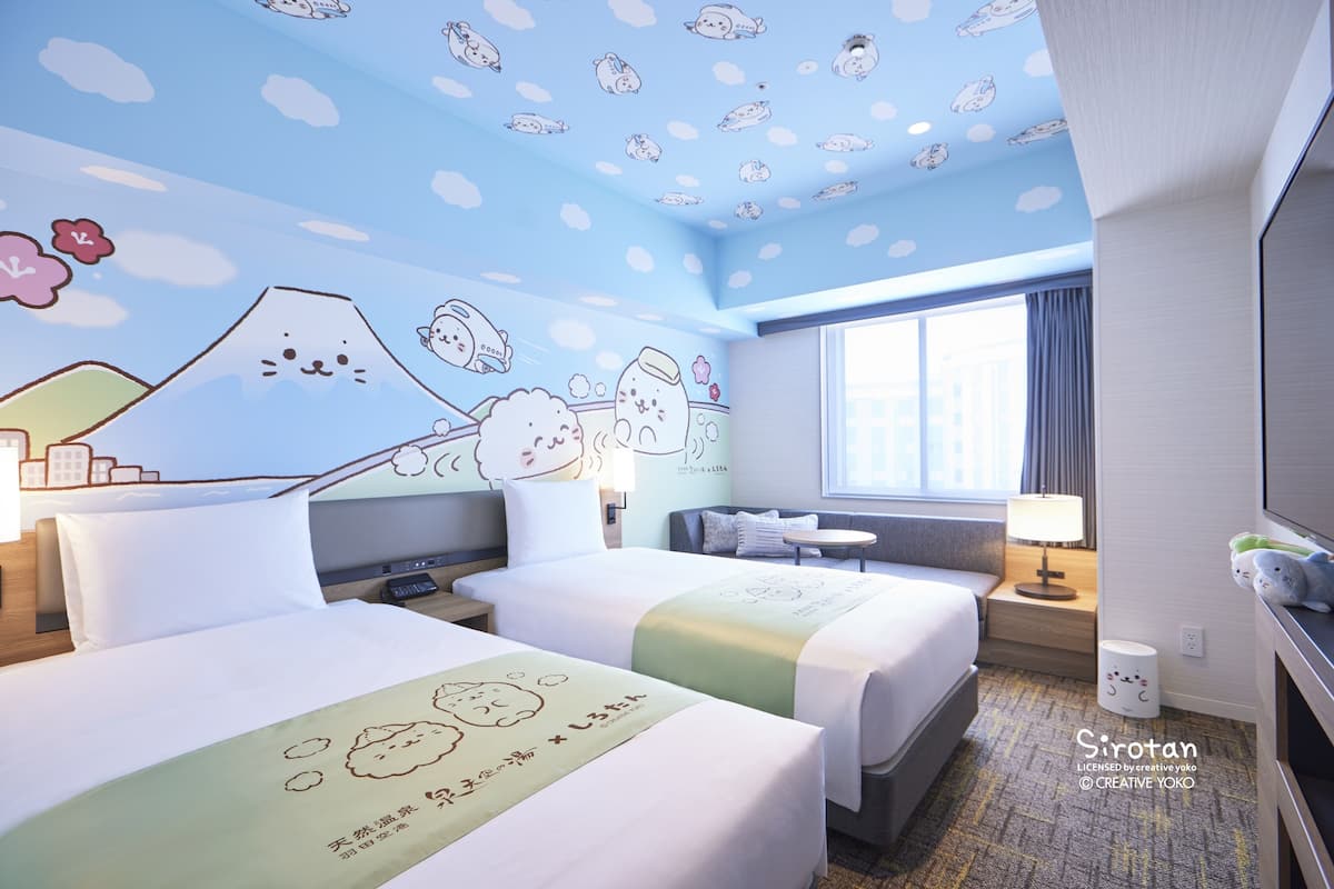 Ein Hotelzimmer mit zwei Betten, einem großen Fenster und einer Deckenmalerei mit Zeichentrickfiguren.