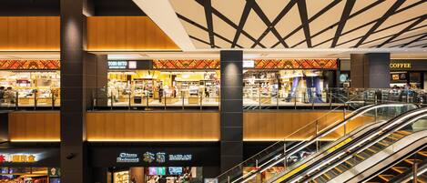 A multi-level shopping mall with escalators, various retail stores, and a prominent coffee shop.