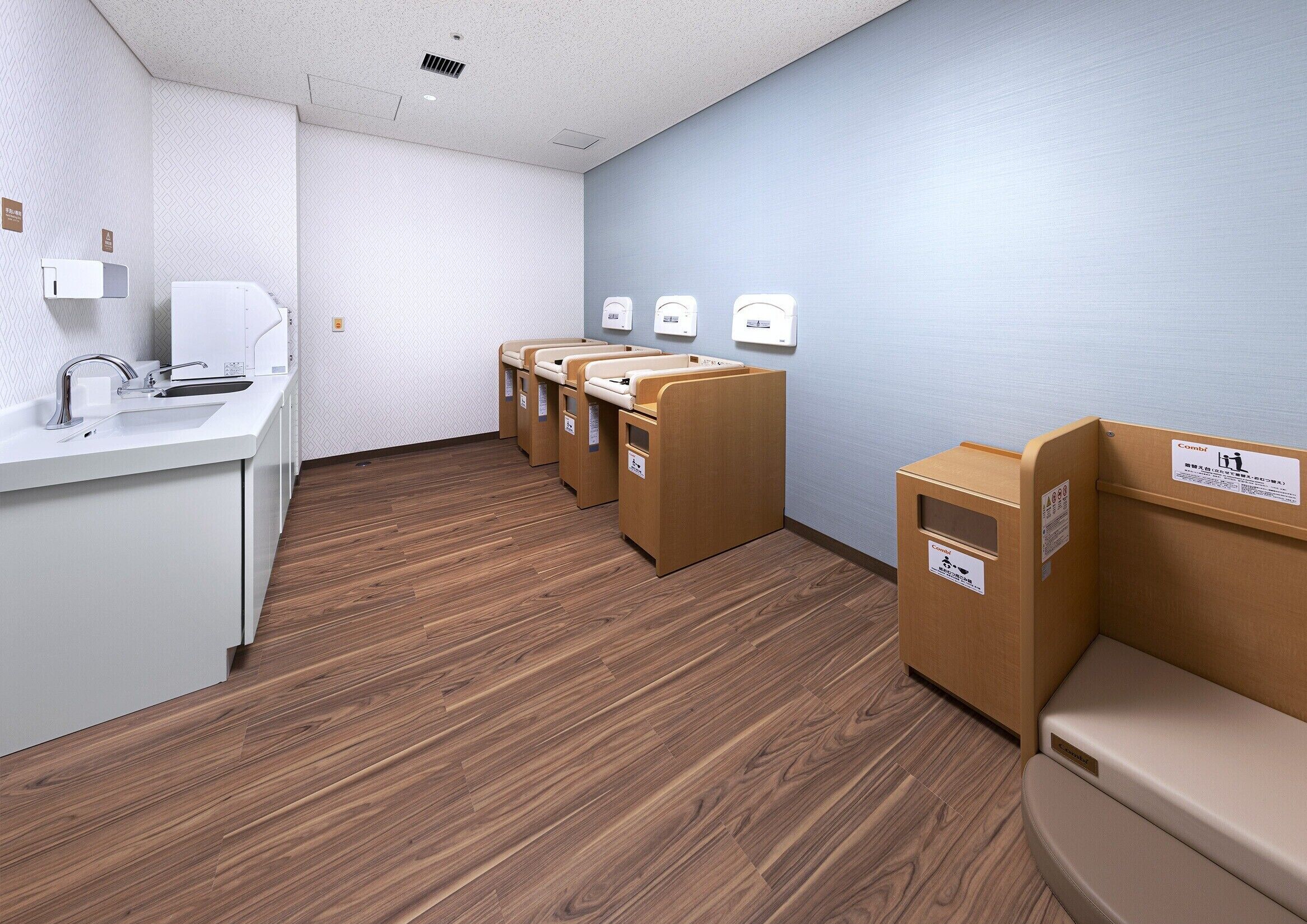 A restroom with a sink, three toilets, and a trash bin.
