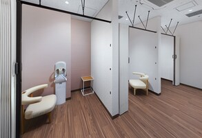 A modern, clean room with wooden flooring, a reception desk, and a seating area with a chair and a small table.
