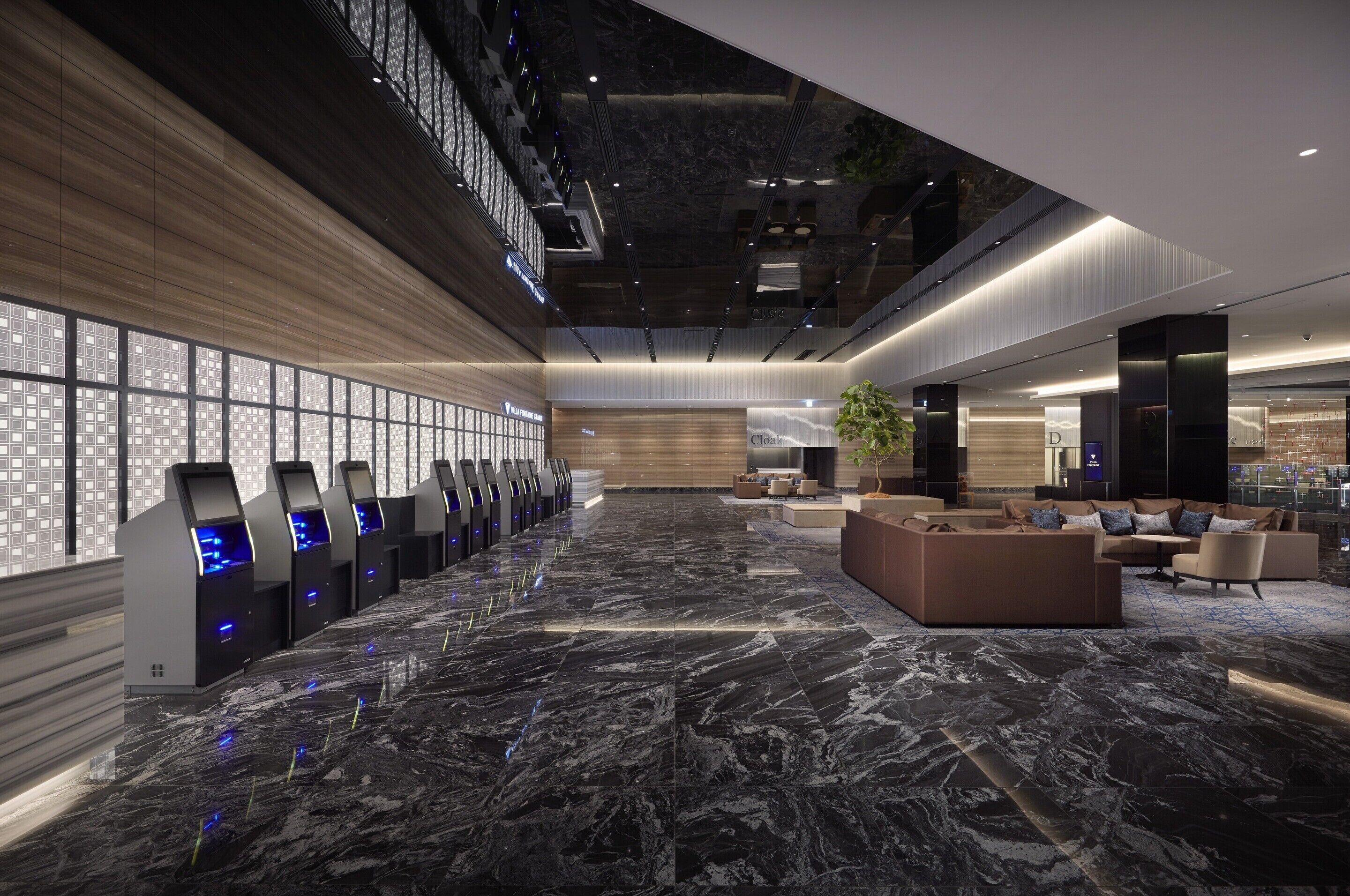 A spacious lobby with a marble floor, a reception desk, seating area, and a large windowed wall.