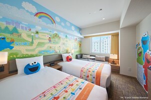 A hotel room with two beds, a mural on the wall, and a window with a view of buildings.