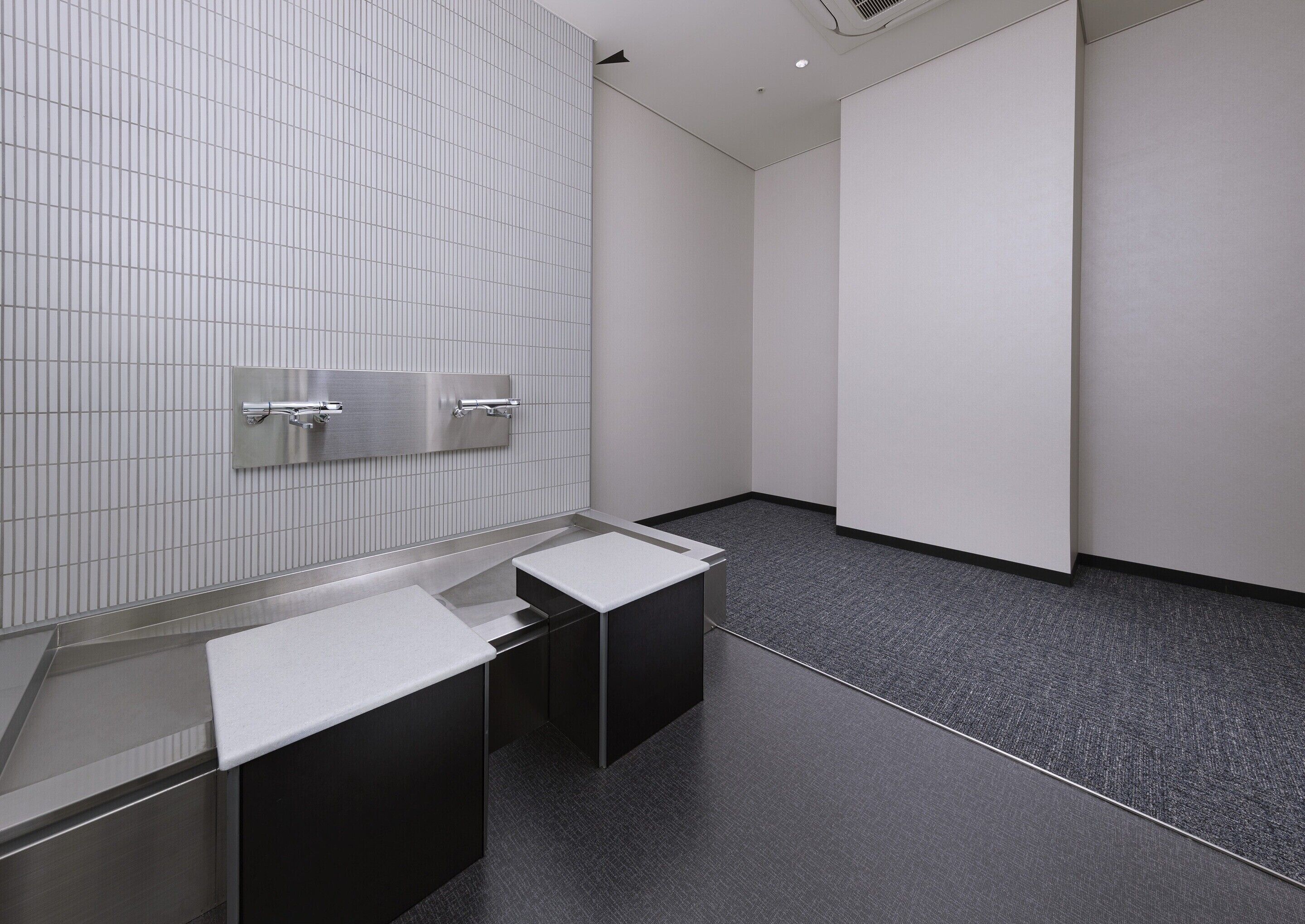 Un baño moderno con pared de azulejos, un secador de manos metálico y suelo negro.