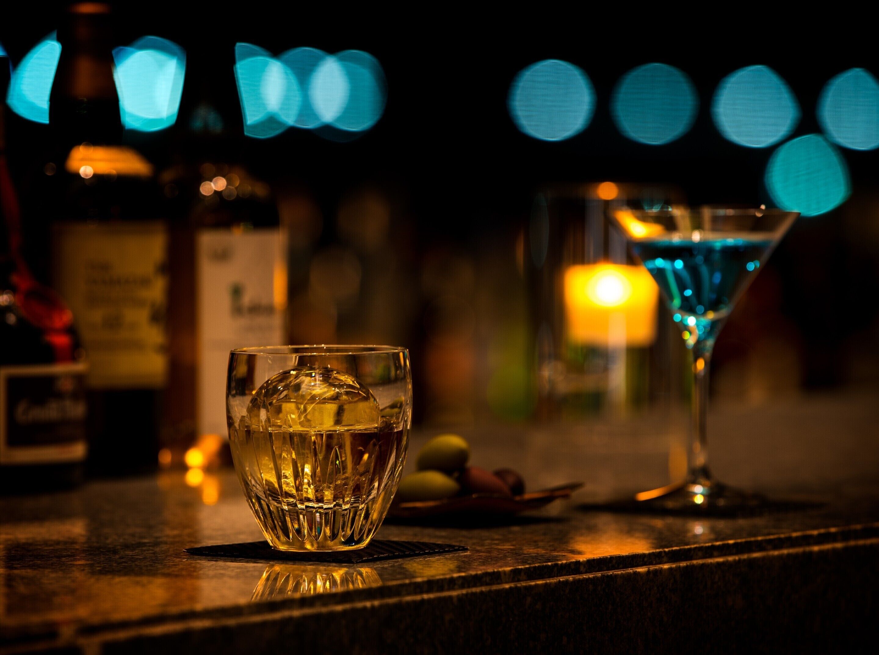 Un bar con una copa de whisky y una copa de martini, con luces de fondo desenfocadas.