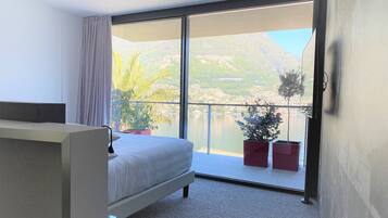 A bedroom with a bed, a large window, and a balcony with potted plants.