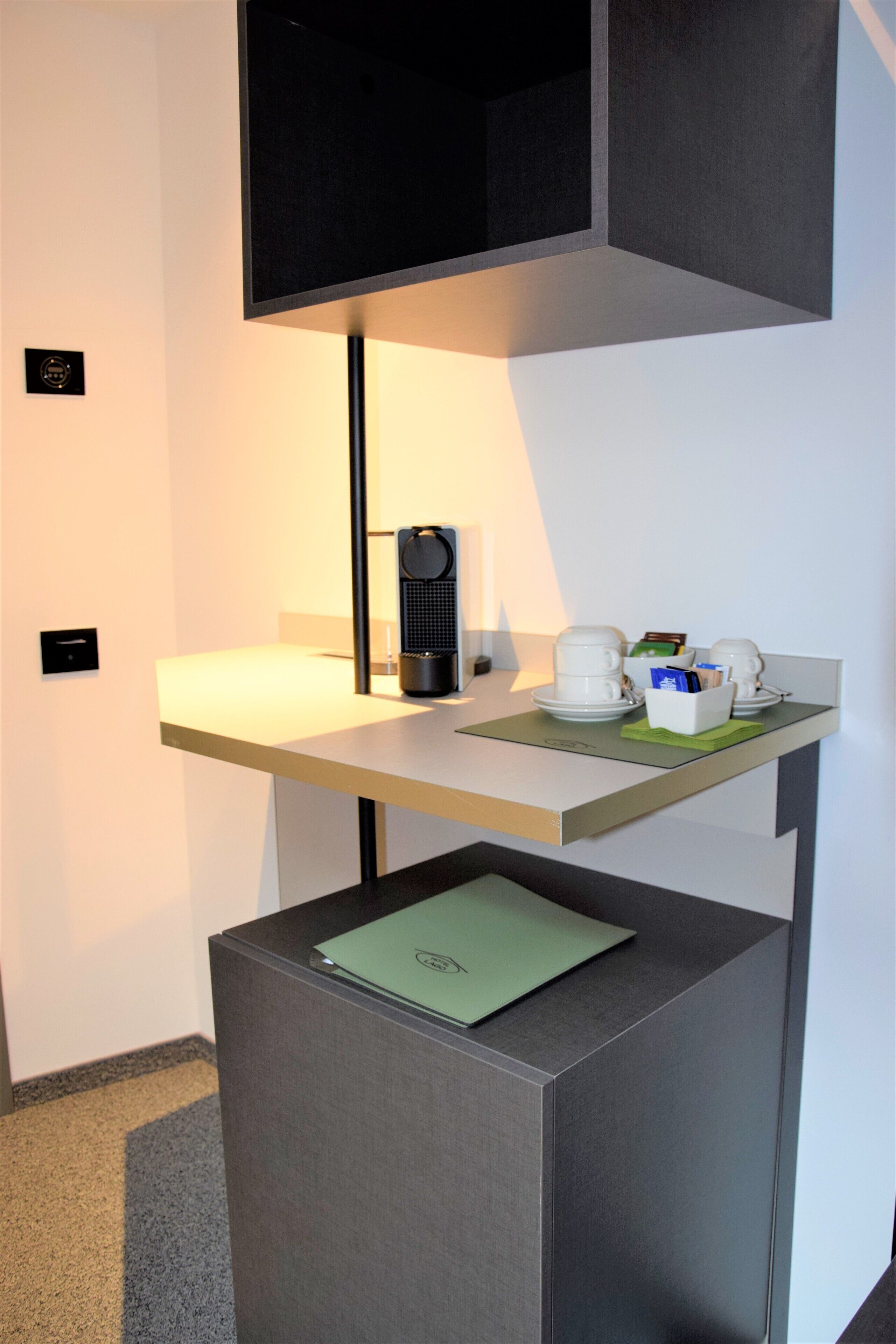 A modern hotel room with a desk, a coffee machine, and a green folder on a cabinet.