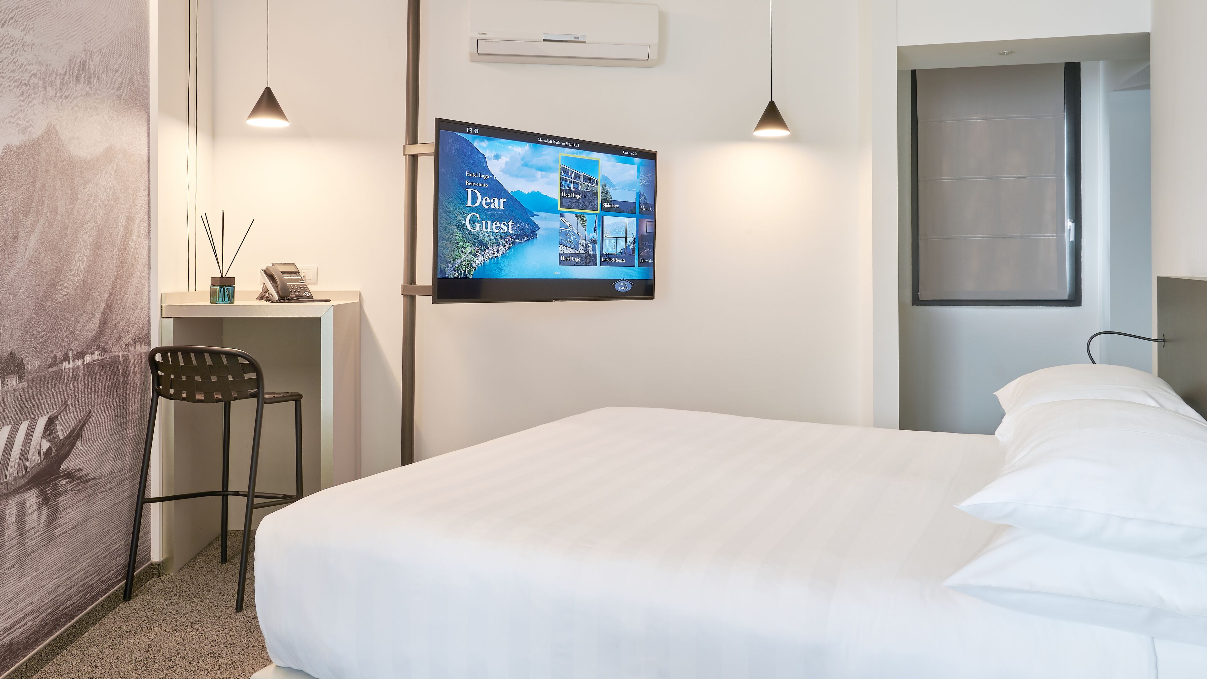 Habitación de hotel con cama, escritorio con teléfono, silla, televisor montado en la pared y puerta.