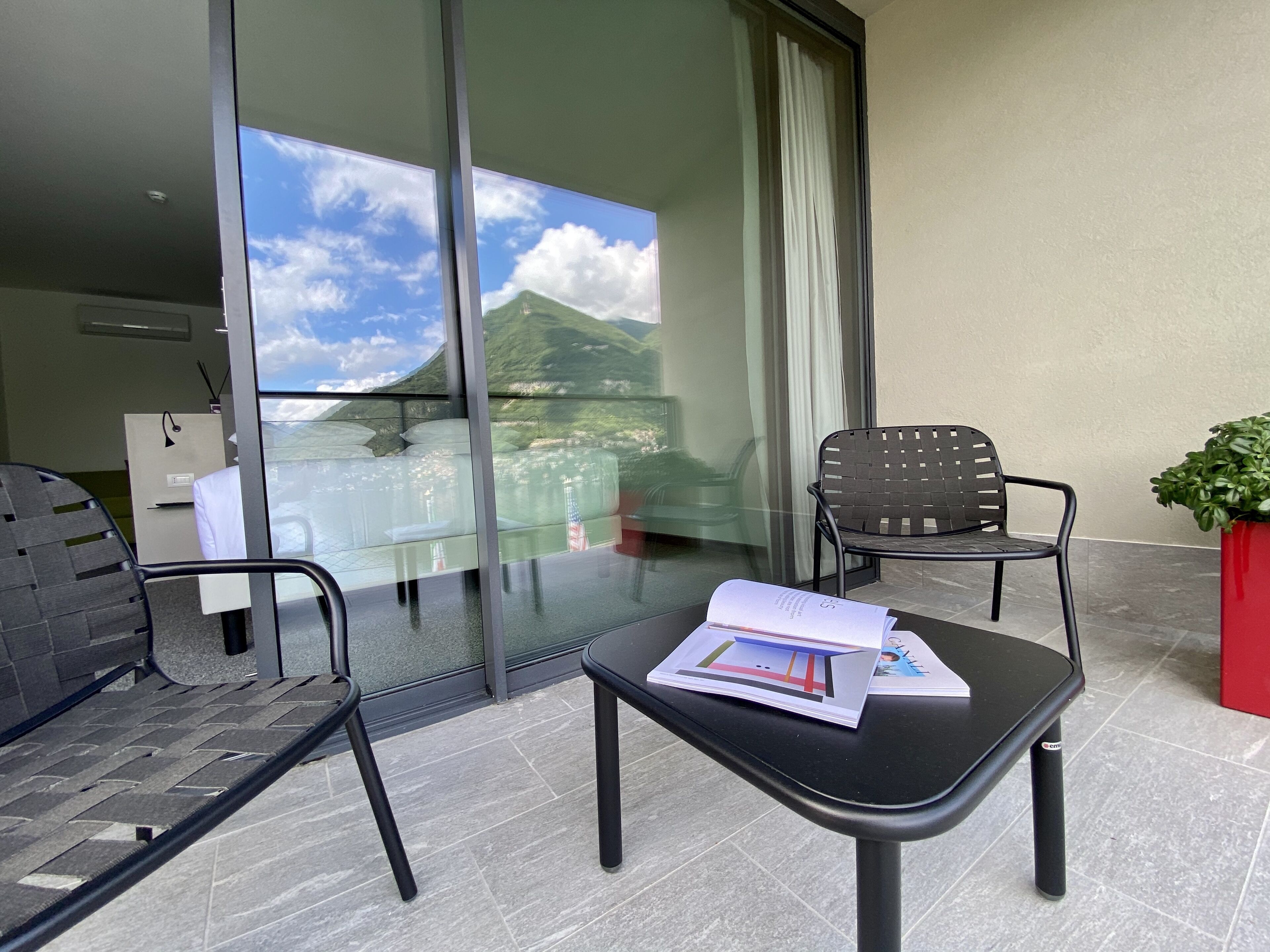 A balcony with a glass door, two chairs, a table with a book, and a potted plant.