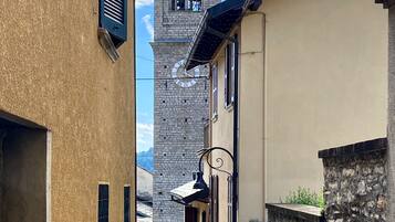 A narrow street with buildings on either side, a clock tower, and a cross on top.