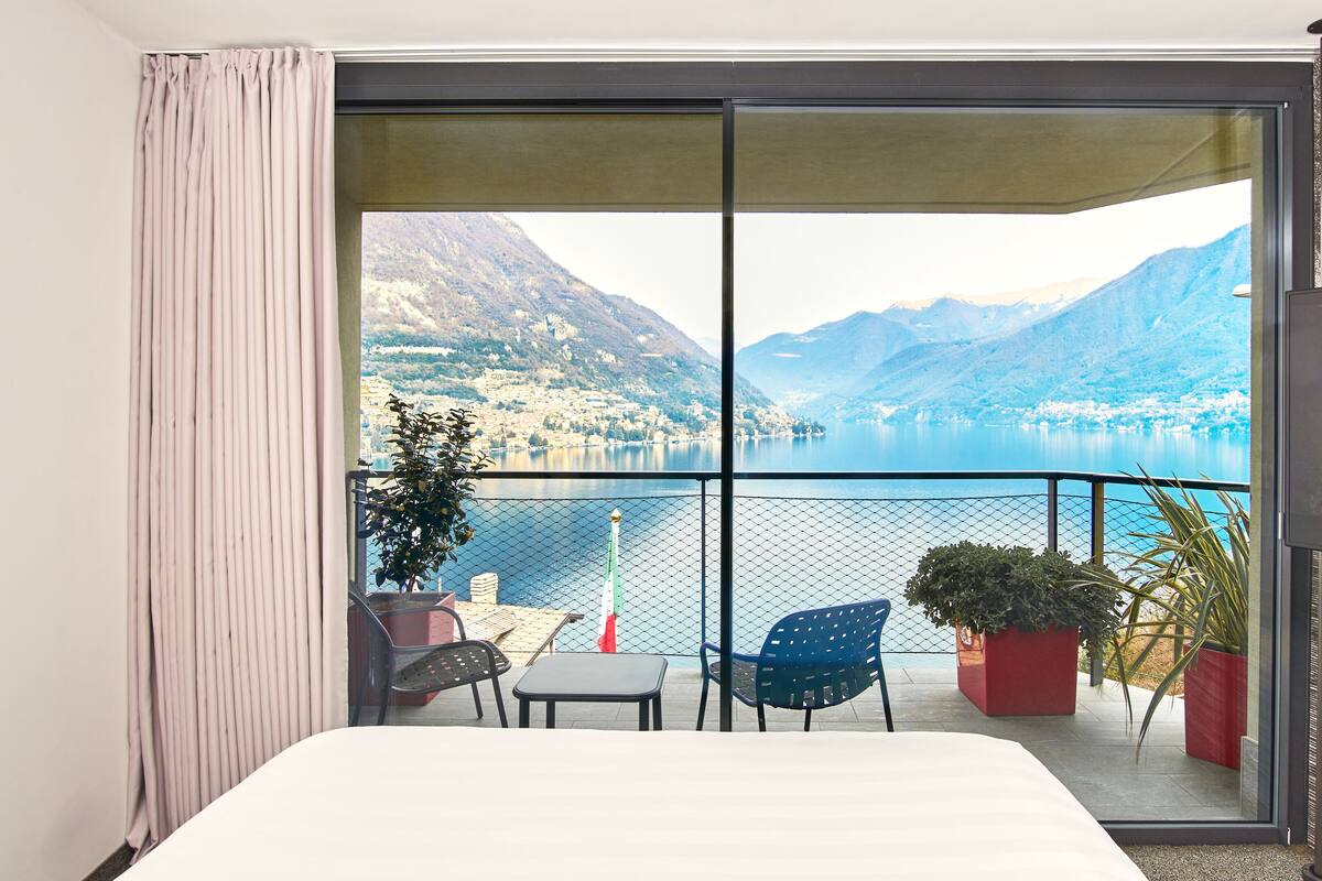 Un balcón con vistas a un lago y montañas, una cama y un cartel de bienvenida.