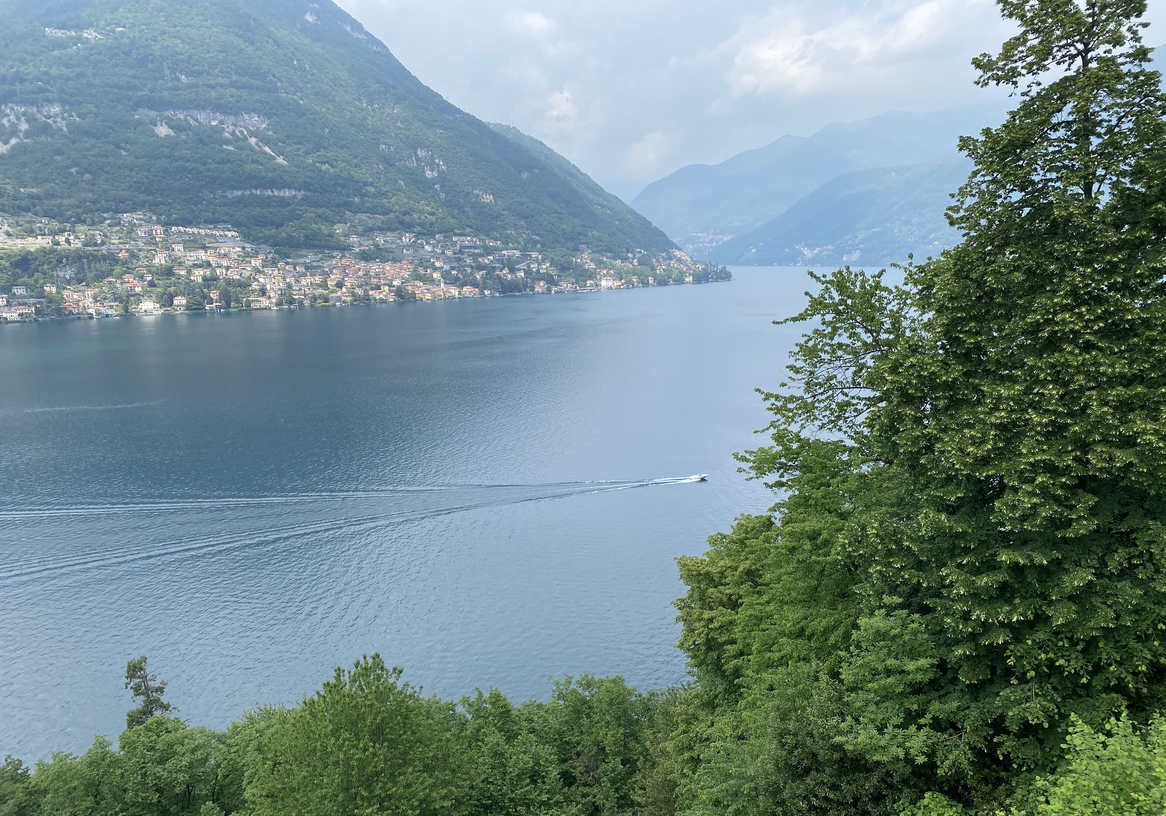 A lake with a boat creating a wake, surrounded by lush green hills and a small town.