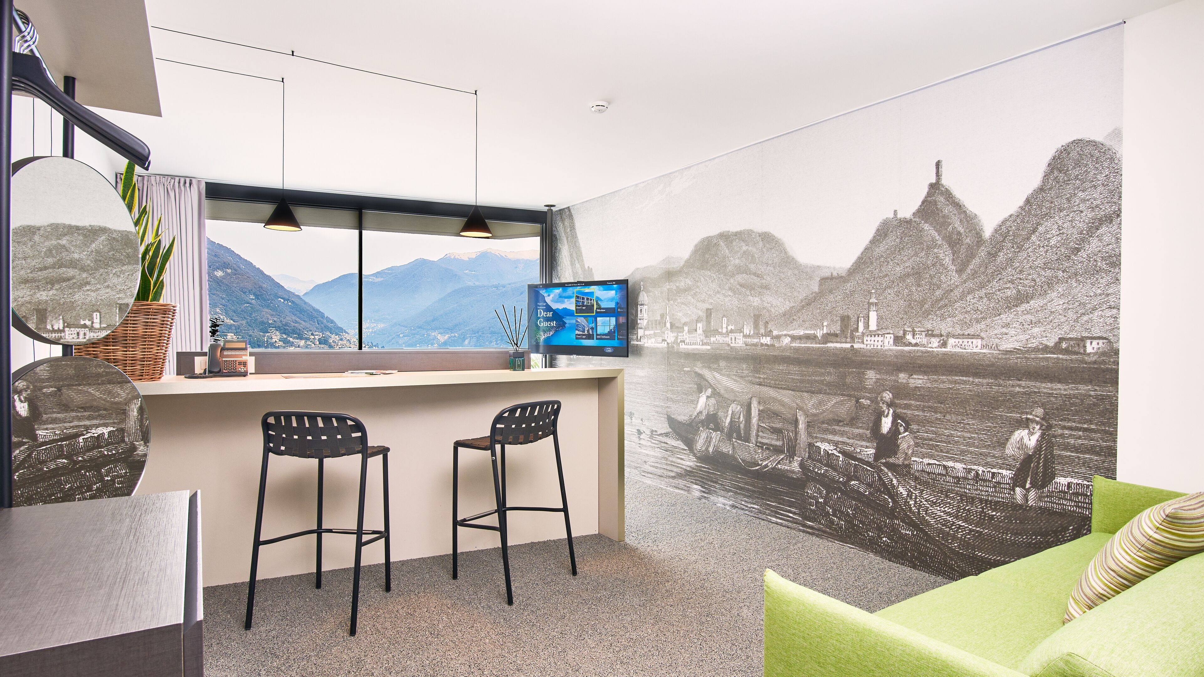 Una habitación moderna con un ventanal grande, un escritorio con dos sillas, un televisor y un mural con una escena fluvial.