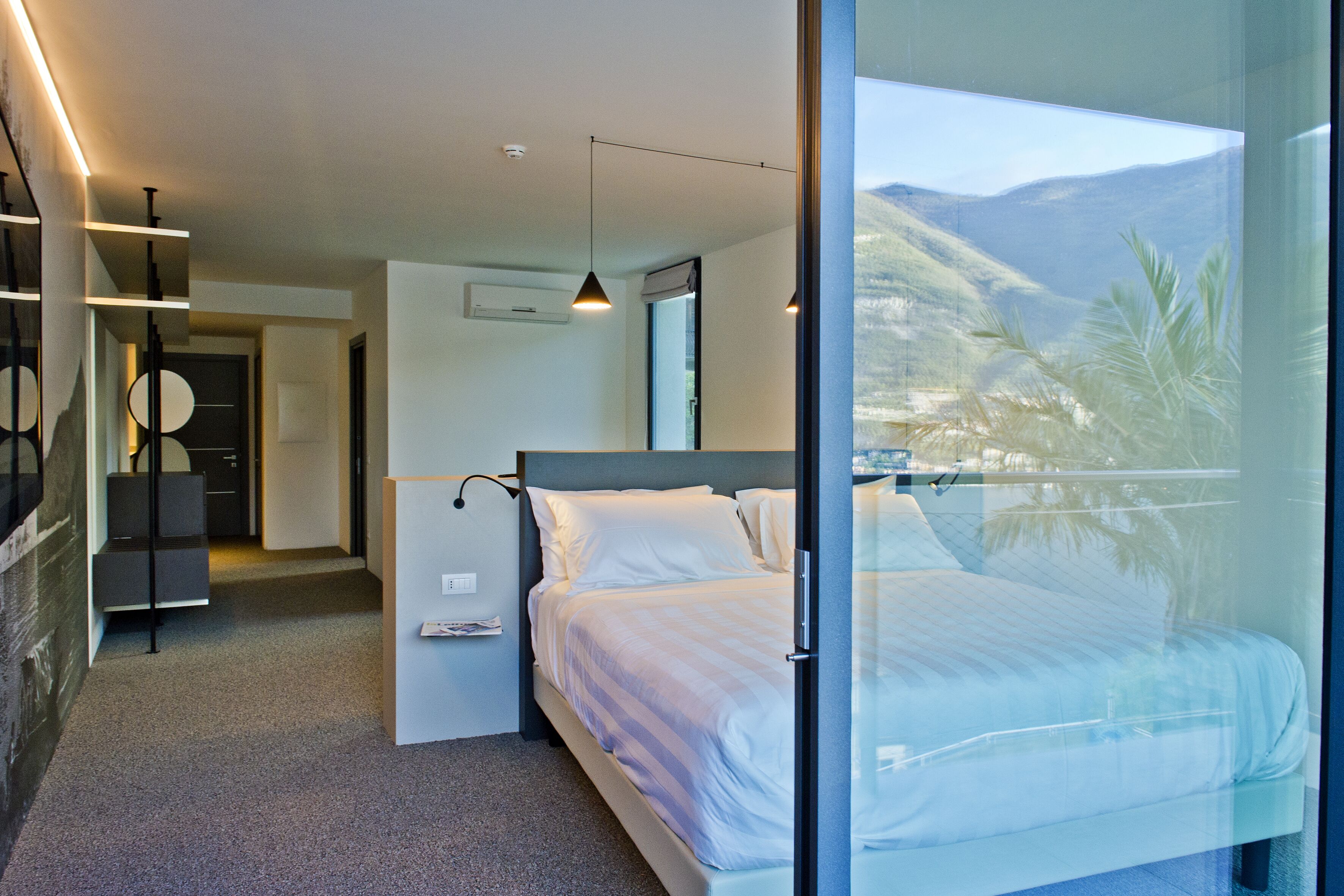 Ein modernes Hotelzimmer mit einem großen Bett, einer Glastrennwand, Bergblick und minimalistischem Design.