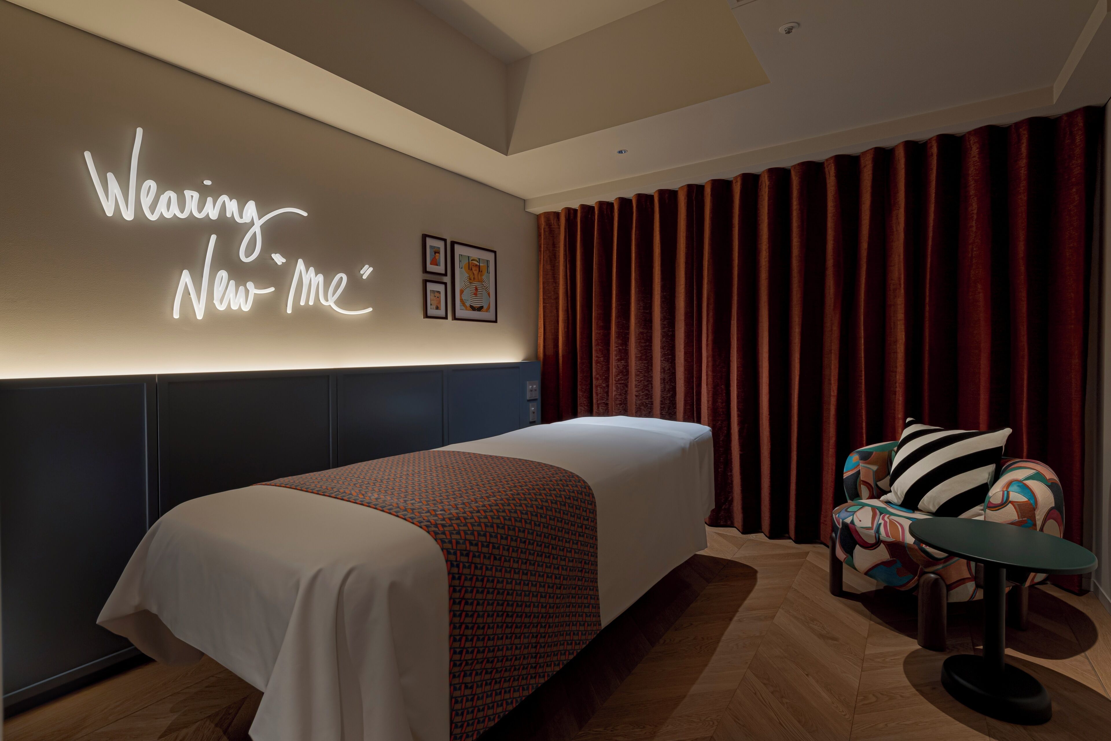 A hotel room with a bed, a wall-mounted light display, a chair, and a table.
