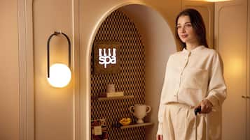 A woman in a white robe standing in a spa-themed room with a checkered wall, a spa sign, and a circular light fixture.
