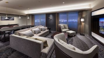 A modern hotel room with a large sofa, a smaller sofa, a chair, a desk, and a TV screen.