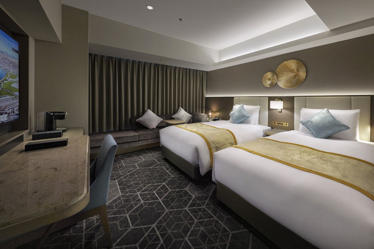 A hotel room with two beds, a desk, and a TV.