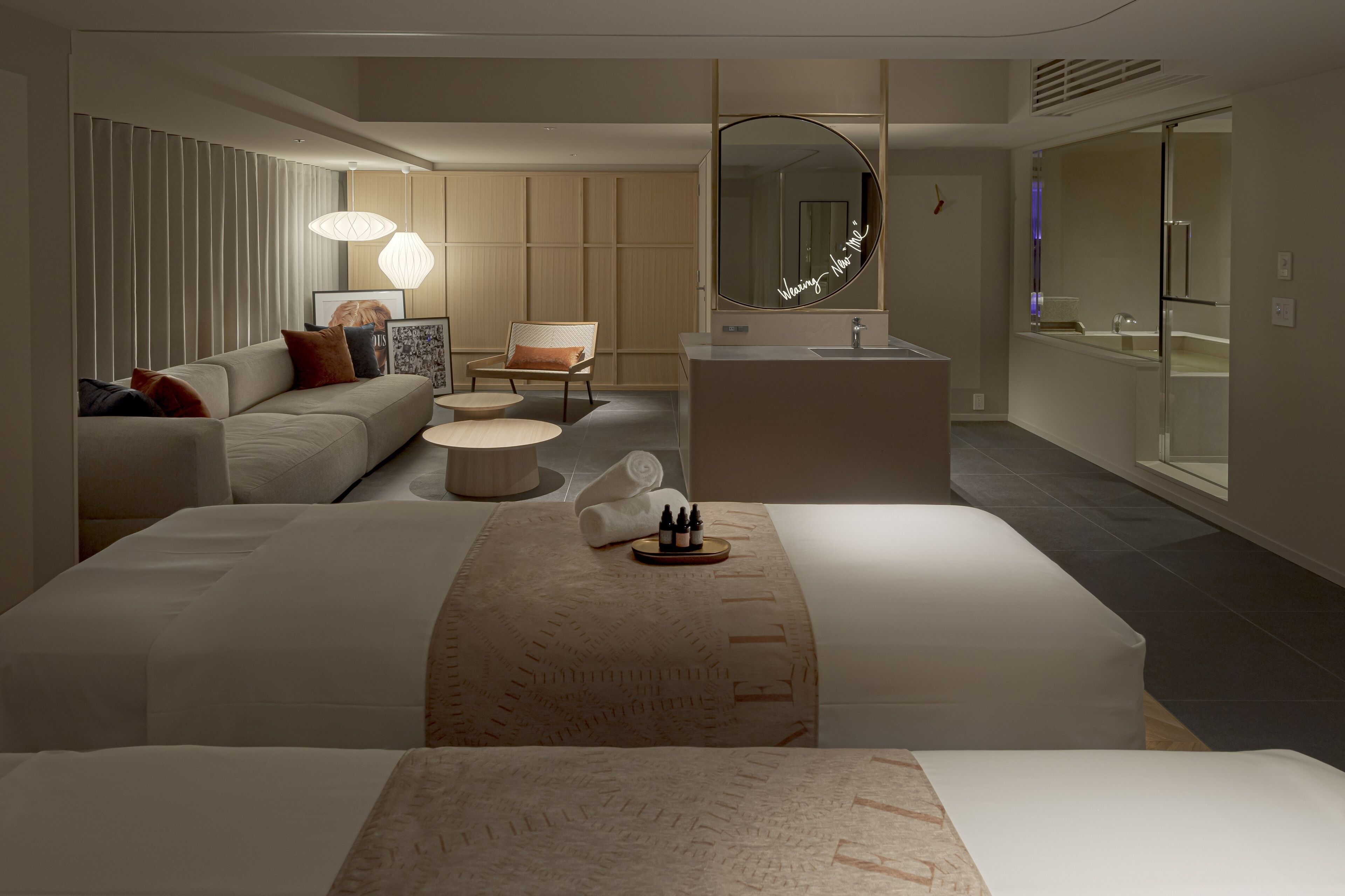 Une chambre d’hôtel moderne avec un grand lit, un canapé, une petite table ronde, un miroir et une salle de bain avec baignoire.