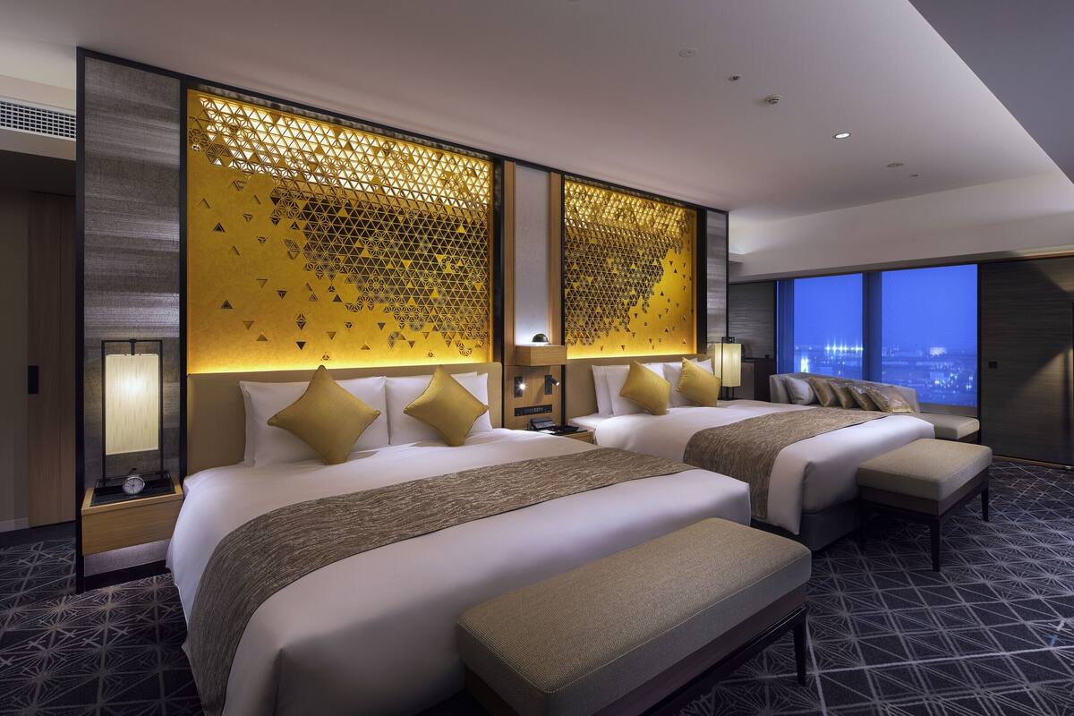A modern hotel room with two large beds, a city view, and a decorative wall panel.