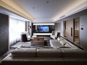 A modern hotel room with a large flat-screen TV, a sofa, a coffee table, and a view of the cityscape through the window.