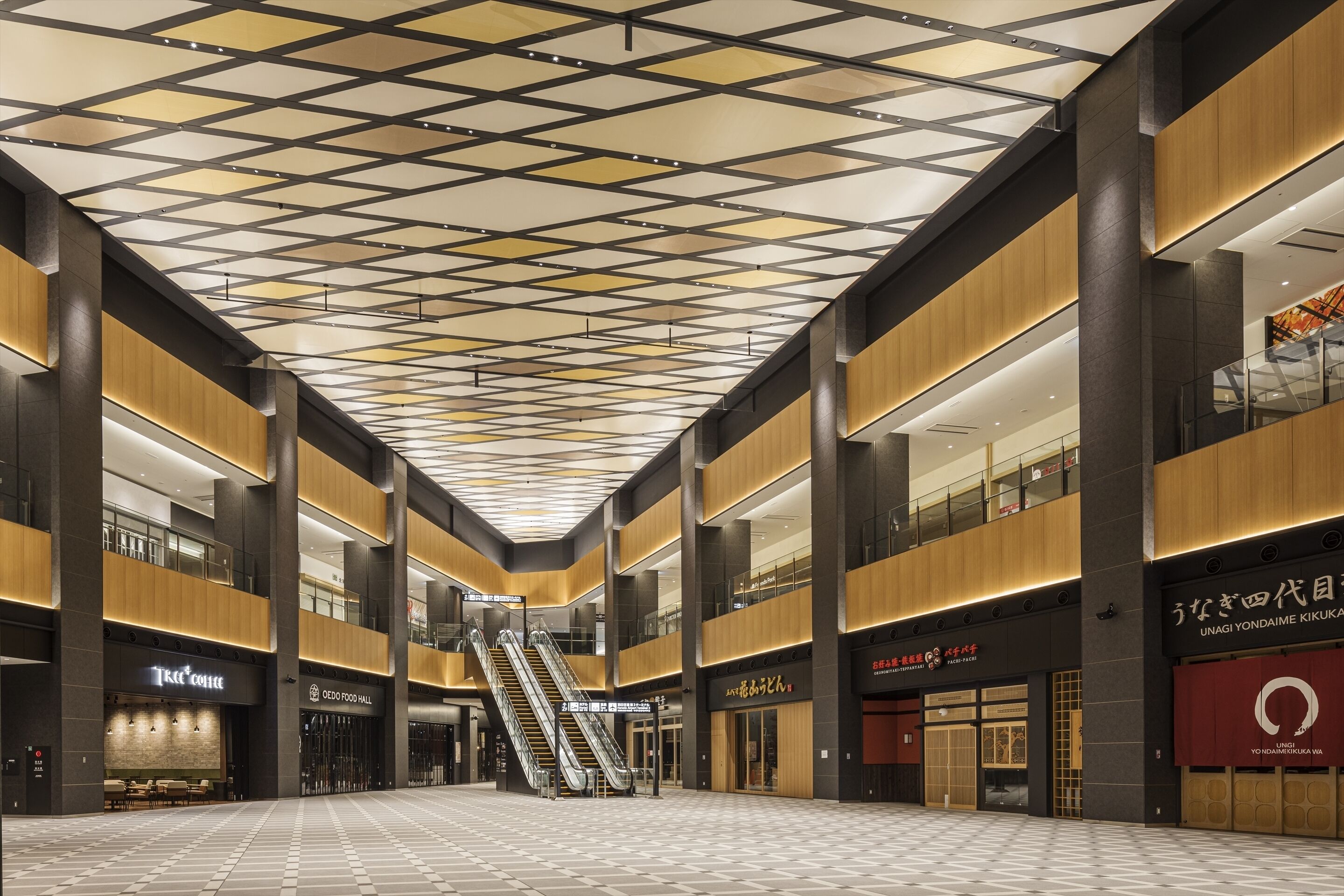A spacious indoor area with a high ceiling featuring a geometric pattern, multiple levels with balconies, and various commercial establishments including a coffee shop and a food hall.