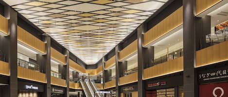 A spacious indoor area with a high ceiling featuring a geometric pattern, multiple levels with balconies, and various commercial establishments including a coffee shop and a food hall.