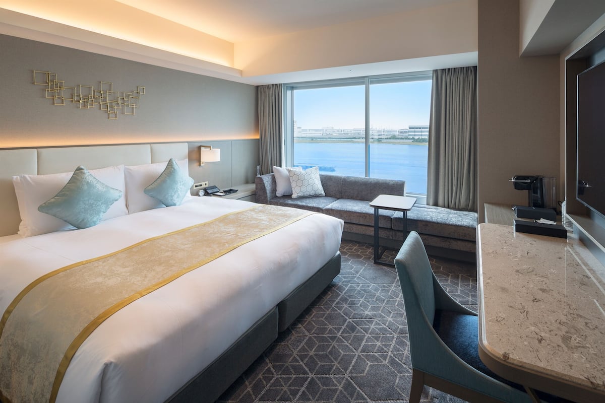 A hotel room with a large bed, a sofa, a small table, and a view of the water.