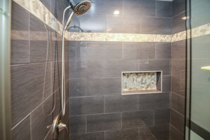 A shower area with dark tiles and a stone accent wall.
