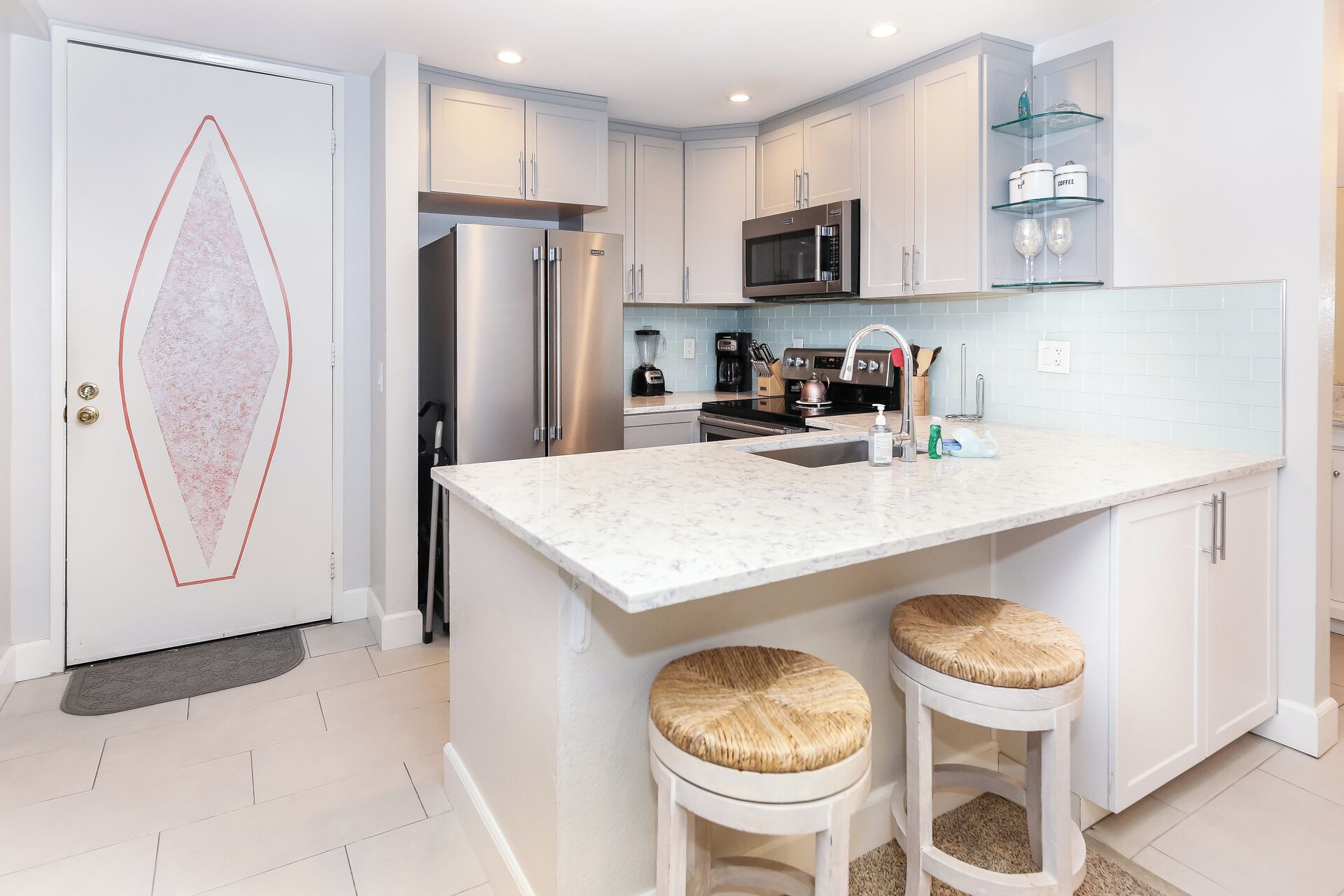 A modern kitchen with white cabinetry, stainless steel appliances, a marble countertop, and two stools.