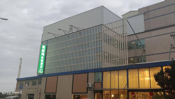 A hotel with a modern facade, large windows, and a prominent green sign on the side.
