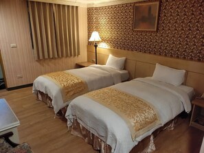 A hotel room with two beds, a nightstand with a lamp, a wooden floor, and a patterned wall.