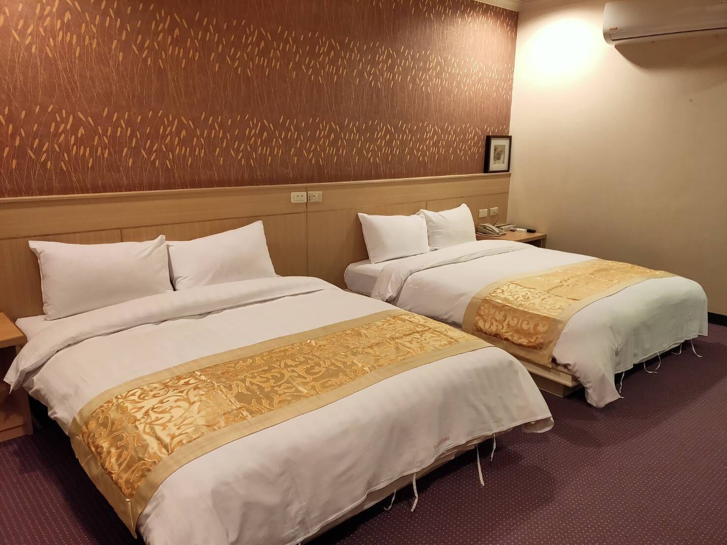 A hotel room with two beds, each with white bedding and a decorative gold trim.