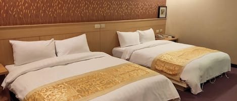 Quarto de hotel com duas camas, cada uma com roupa de cama branca e detalhe dourado decorativo.