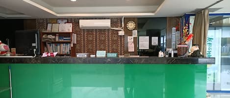 A reception desk with a green counter, a clock, and various informational signs.