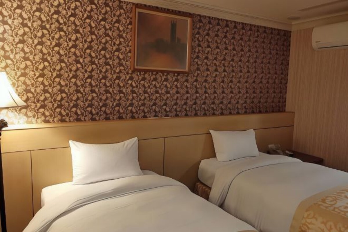 Habitación de hotel con dos camas, un papel tapiz estampado, un cuadro en la pared y un equipo de aire acondicionado.