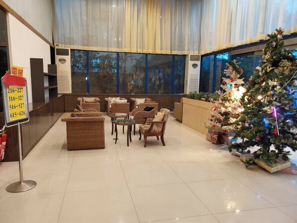 A lobby with wicker furniture, a Christmas tree, and a large window with a view of palm trees. - Melody Hawaii Hotel (Taitung)