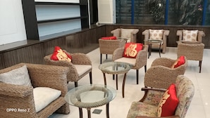 A seating area with wicker furniture and glass tables, featuring red and beige cushions.