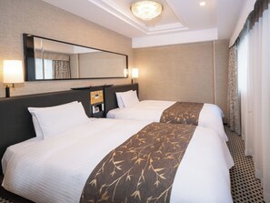 A hotel room with two beds, a large mirror, a control panel, and a patterned bed runner.