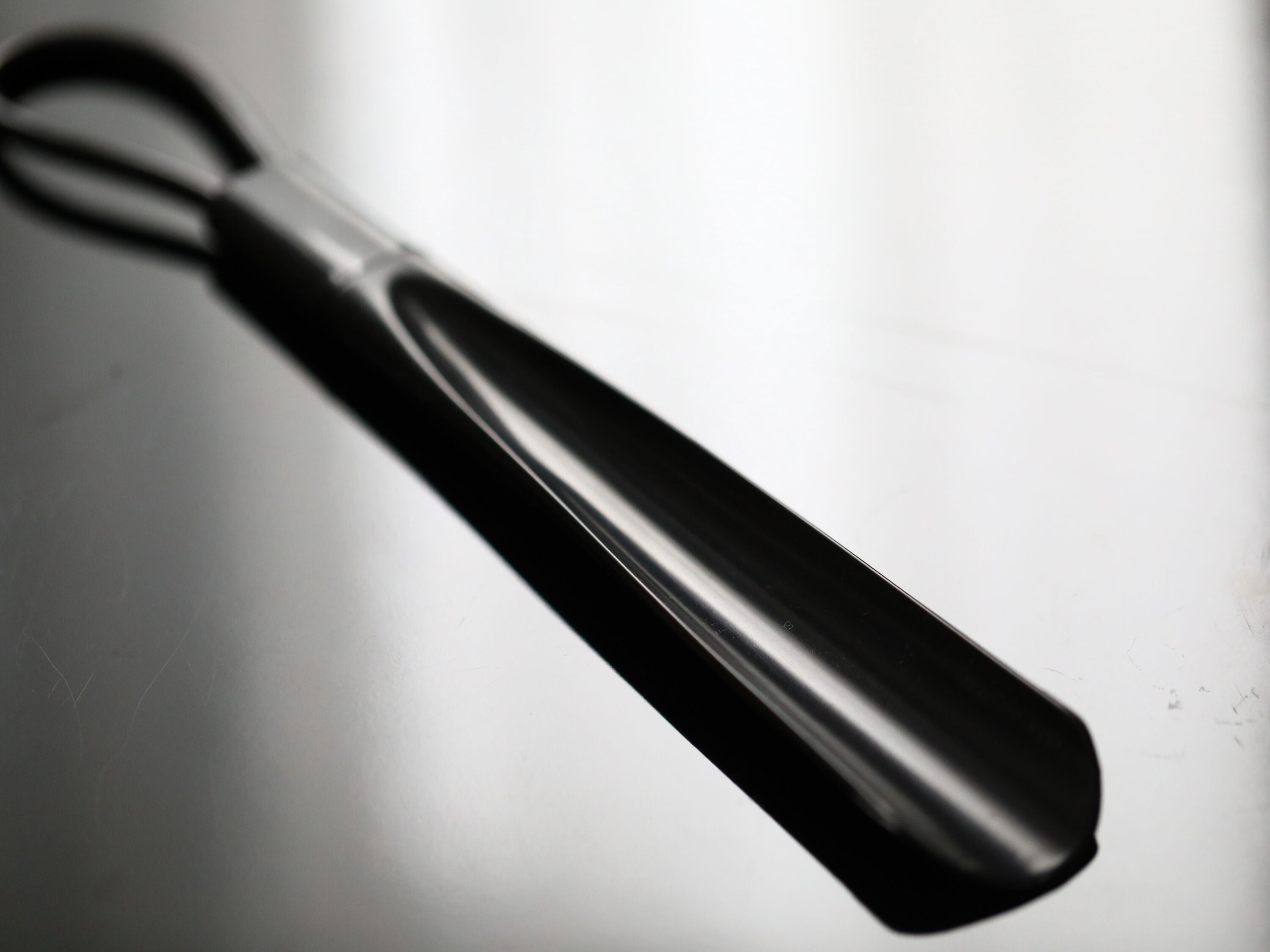 Ein schwarz-weißes Foto eines metallischen Gegenstands mit gebogenem Griff, möglicherweise ein Werkzeug oder ein Utensil, auf einer reflektierenden Oberfläche.