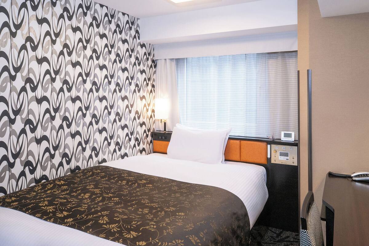 Une chambre d’hôtel avec un lit, une table de chevet, une lampe et une fenêtre avec des rideaux.