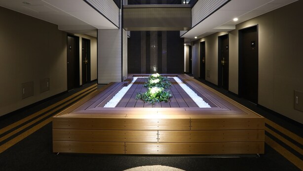 Een moderne hotelgang met een centraal houten plateau, inbouwverlichting en een dakvenster.