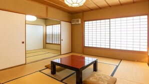 Una habitación japonesa tradicional con suelo de tatami, una mesa de madera baja, un cojín y grandes ventanales con diseños de cuadrícula.
